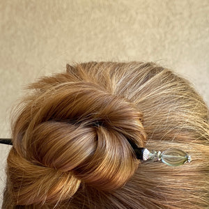 A woman wears a hair bun with one of our Brooke  Hair Sticks made from green -blue ombre Czech glass beads.