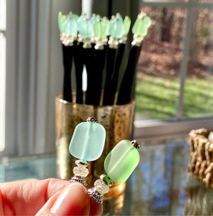 A group of just-made aqua and green Erin Tidal Hair Sticks are drying by a window.